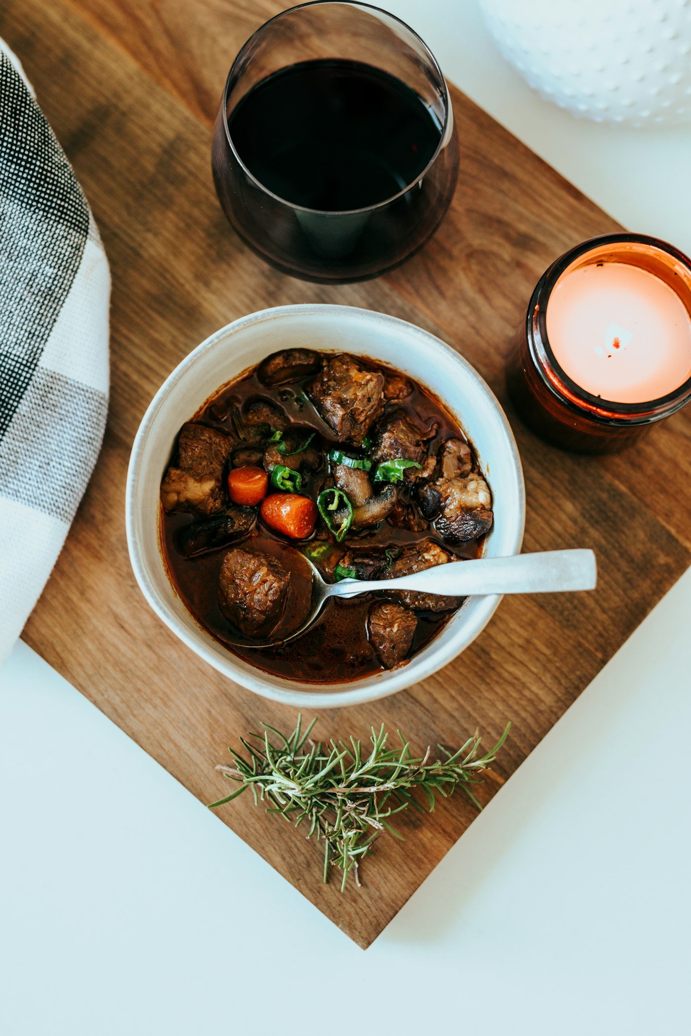 Bol de viande mijotée, vin rouge et bougie sur une planche