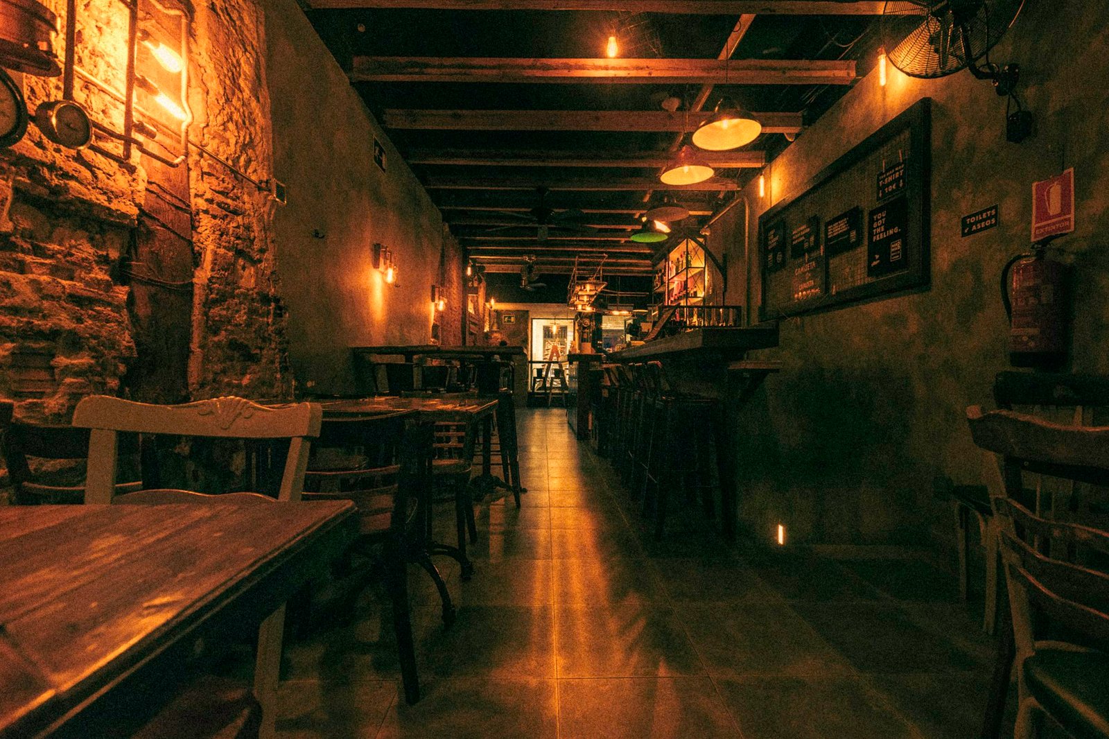 Salle rustique aux murs de pierre et aux poutres, éclairée de lampes